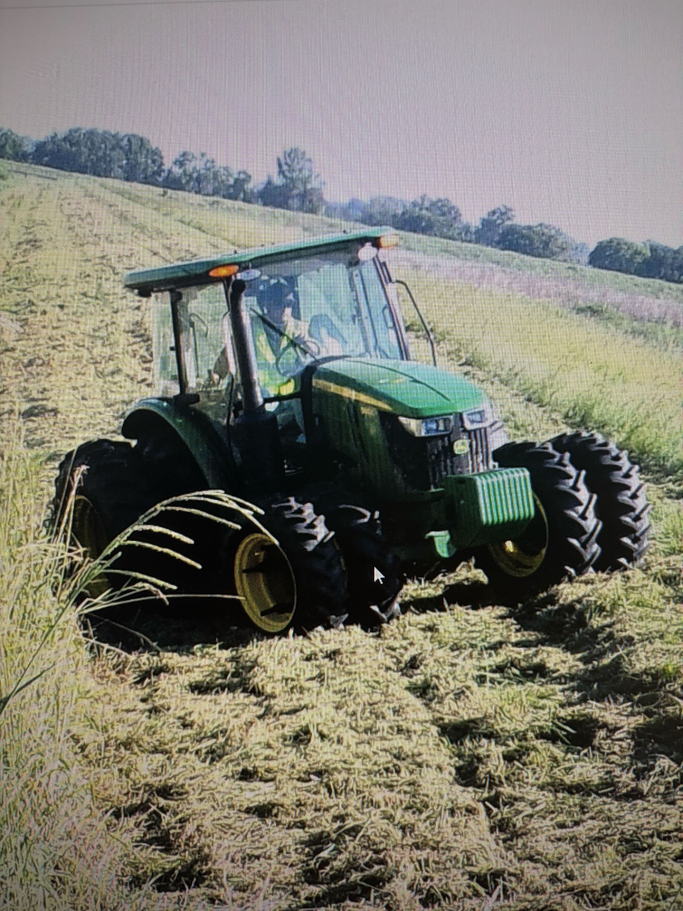 John Deere tractor mowing a large sloped field